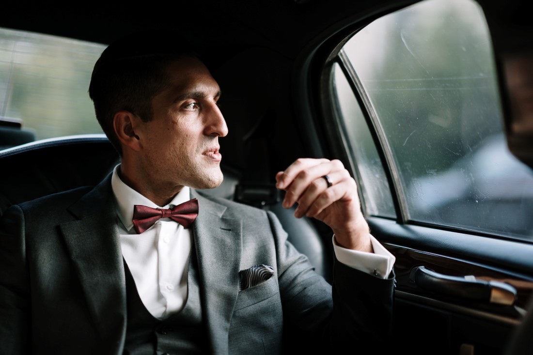 Groom wearing Indichino grey suit sits in limousine by Ross Kyker Photography