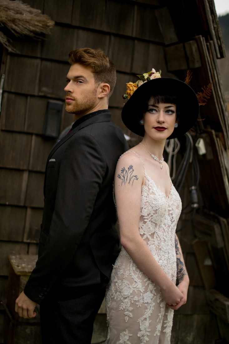 Tattooed Newlyweds stand back to back in front of cabin in Vancouver