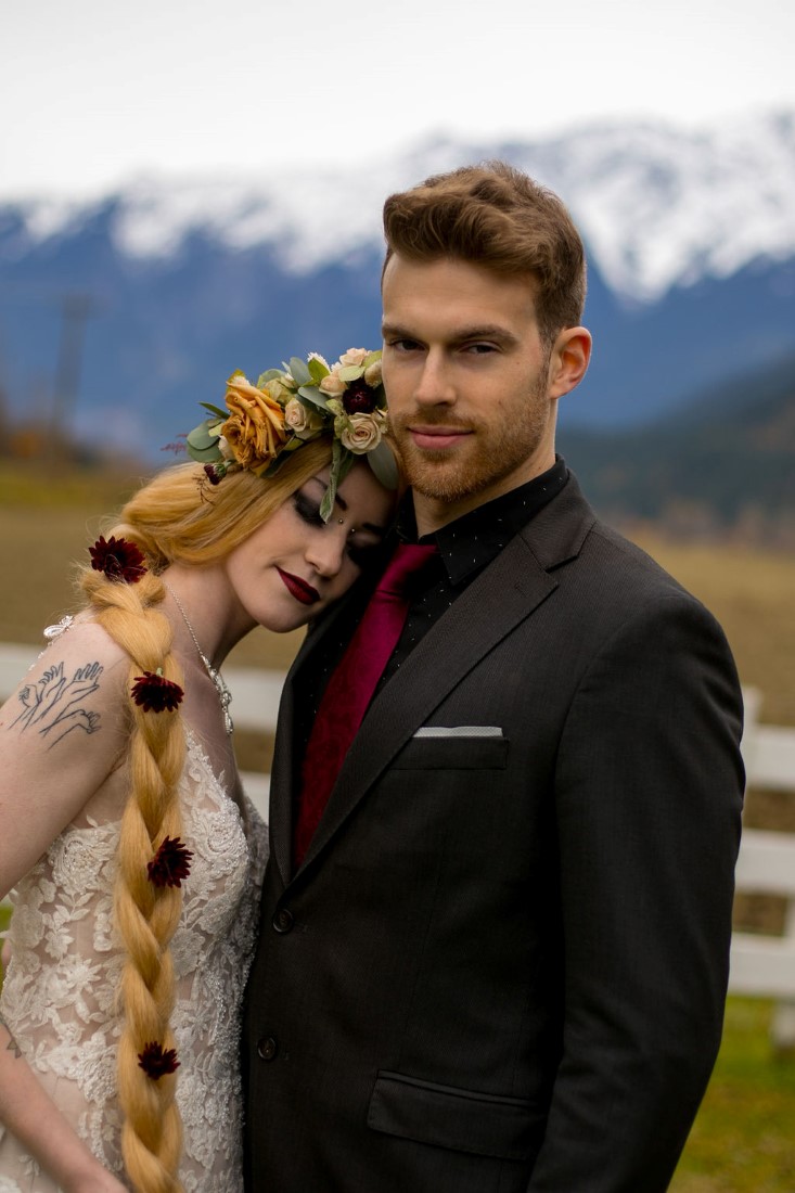 Bride leans on groom with BC mountains behind them