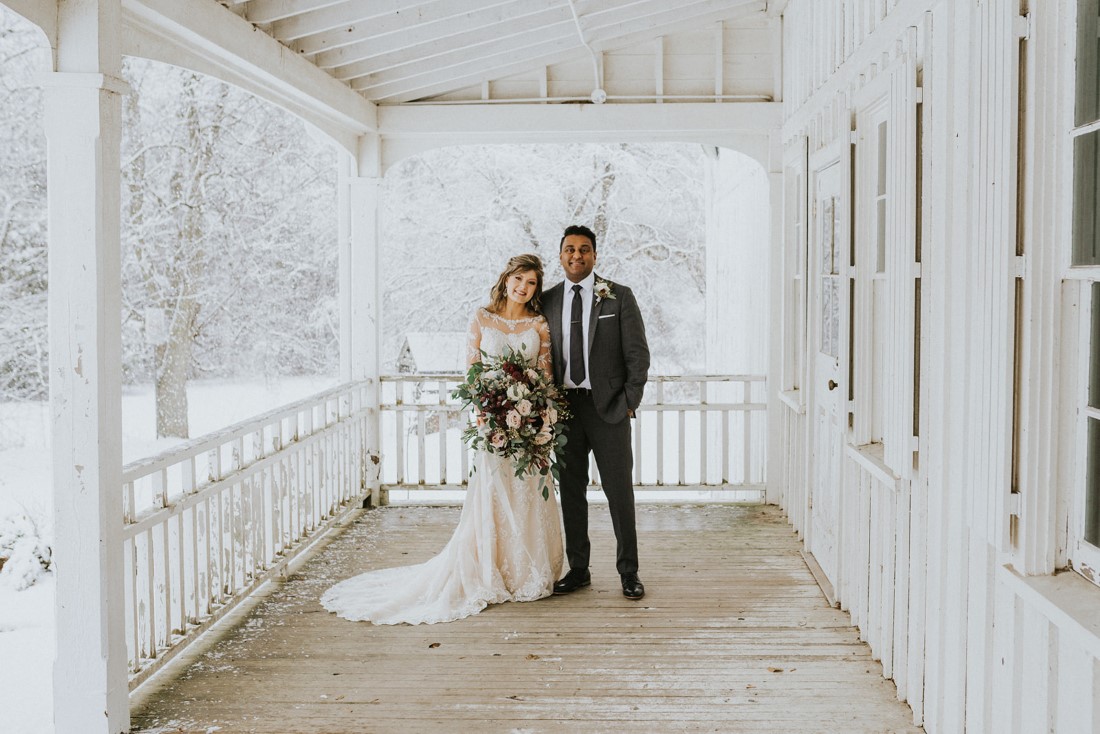 Bride and Groom on Farmhouse porch with snowstorm behind by White Canvas Photo