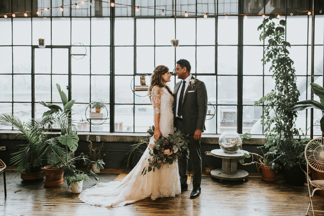 Snowy Urban Fairytale Wedding Couple in front of wall of windows and snow