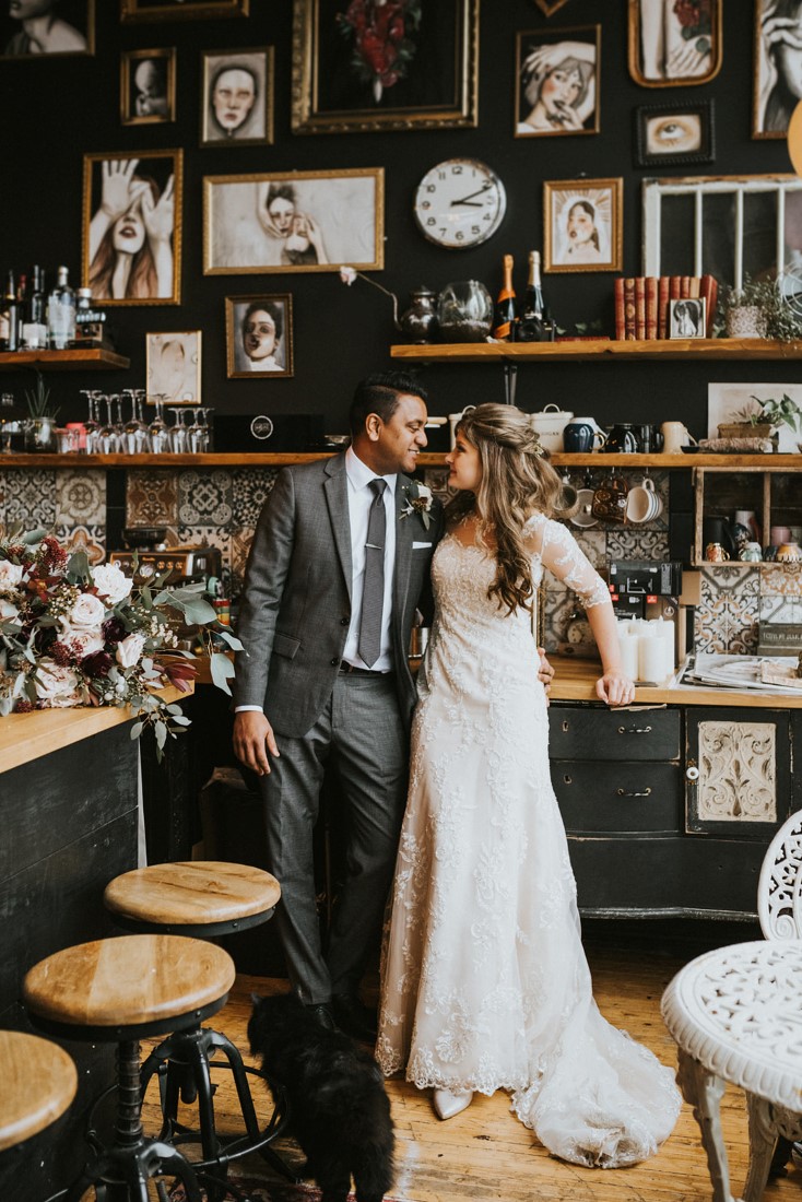 Snowy Urban Fairytale Wedding couple in front of wall of antiques 