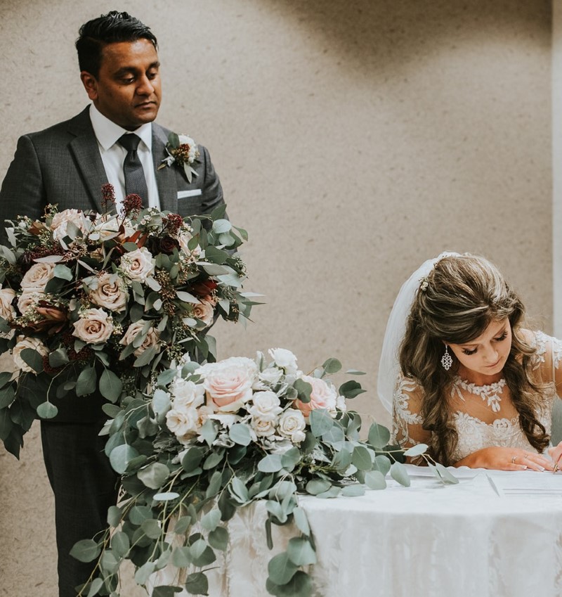 Bride signs register as groom holds her bouquet 