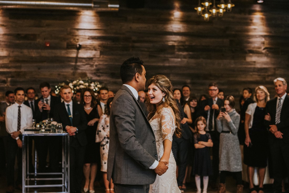 Newlyweds first dance in front of guests in urban warehouse venue 