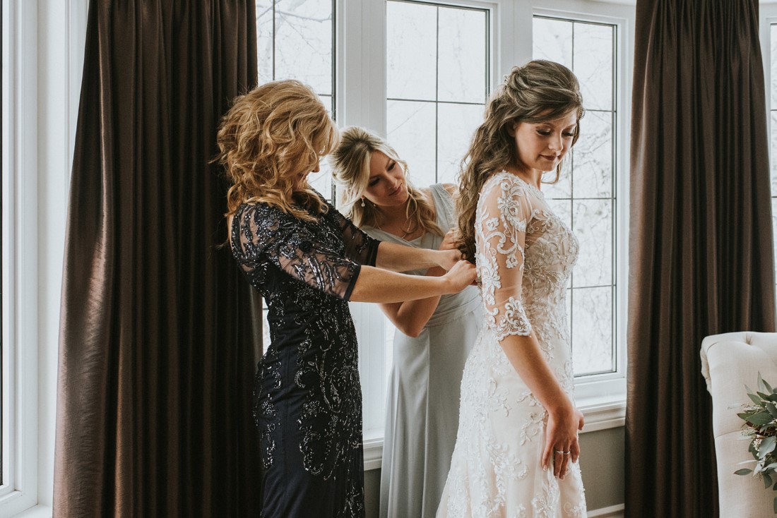 Mother and sister of bride help her with buttons on her Maggie Sottero gown 