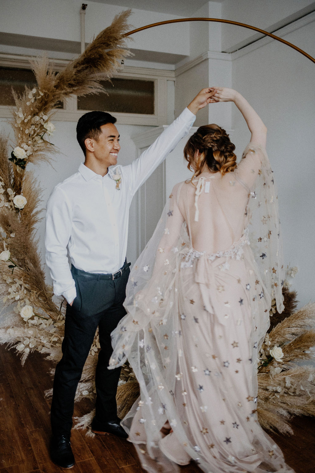 Groom twirls bride wearing dress covered in gold stars by Flutter Dresses