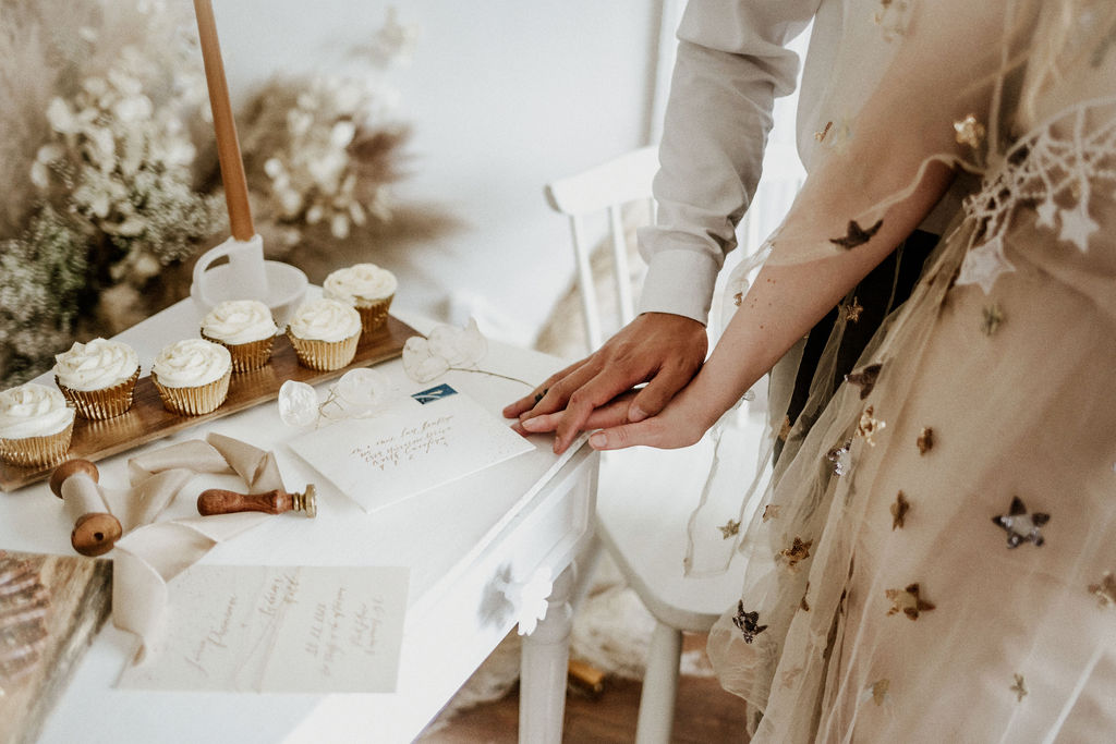 Bride and groom's hands show off wedding rings by cupcakes with white icing on reception table