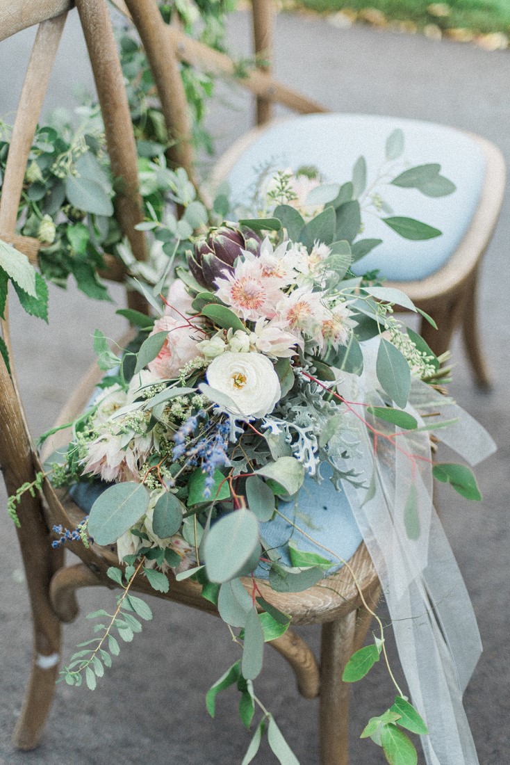 Blush pink flowers and ribbons sit upon blue french chairs