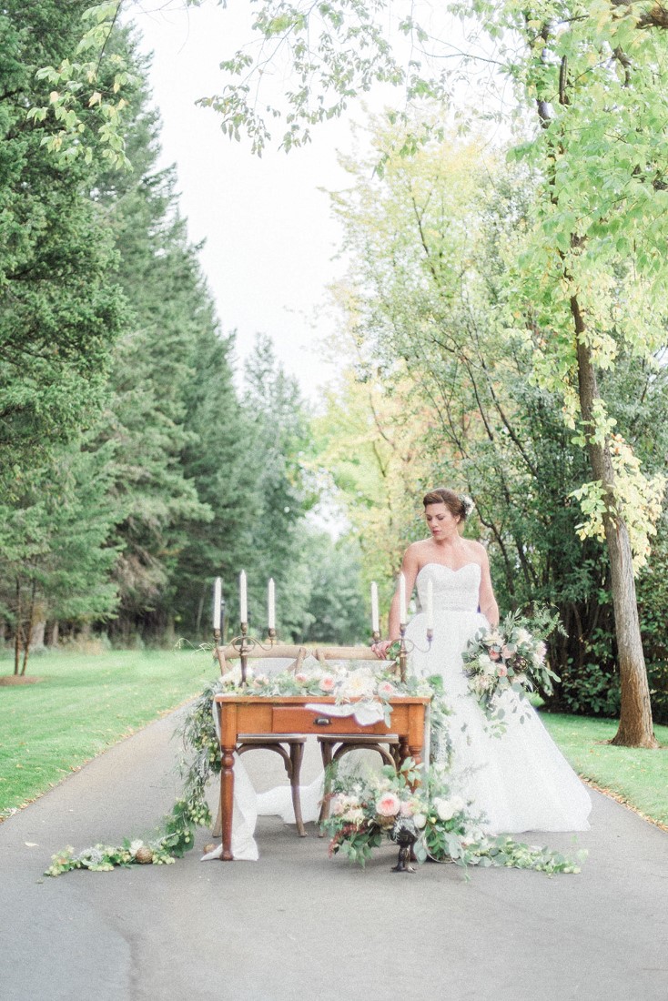 Bride stands on country road beside table filled with wedding decor