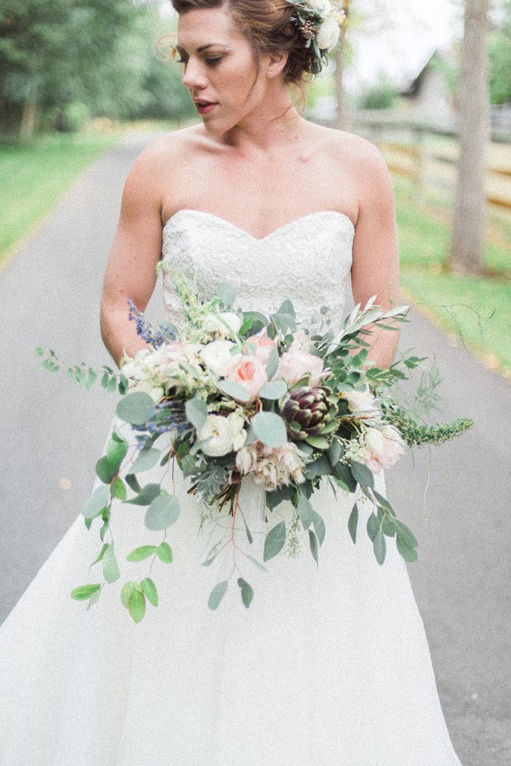 Bride holds bouquet of blush pink and white flowers on country road