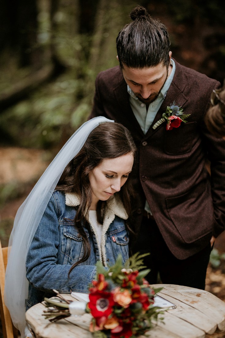 Bride wearing jean jacket signs wedding ceremony papers at Wick Inn Tofino