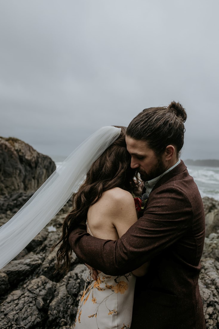 Bride and groom hug on the rocks of Chesterman Beach Tofino