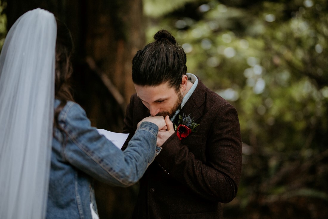 Groom kisses bride's hand during wedding ceremony in Tofino forest