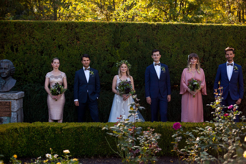 Wedding Party stands against tall green hedge