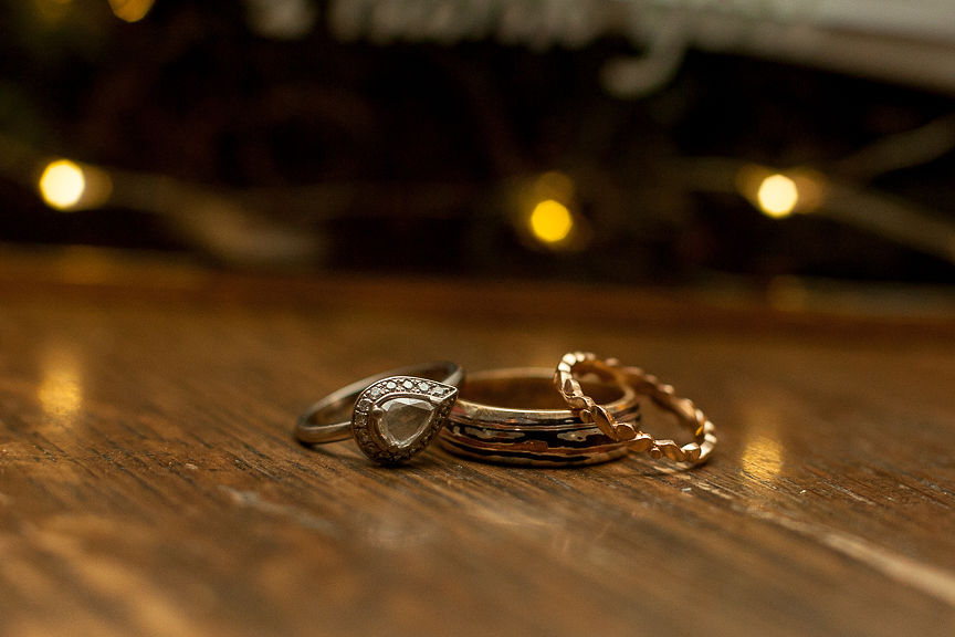 Wedding rings sit on table with twinkle lights behind