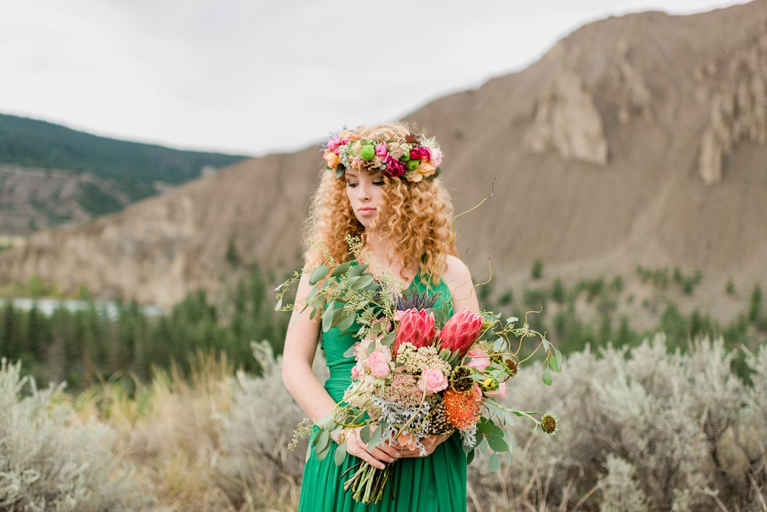 Red haired bride in emerald green dress holds bouquet of colourful flowers