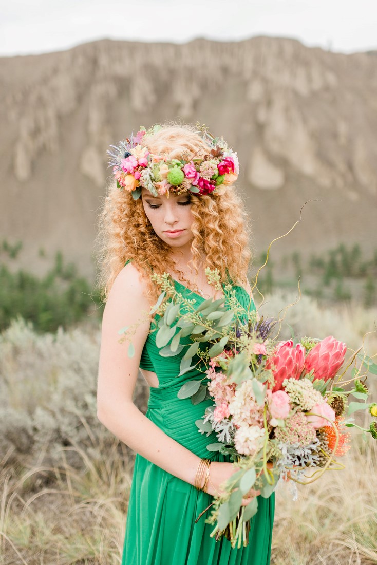 Bride in emerald green dress holds bouquet and wers floral head wreath