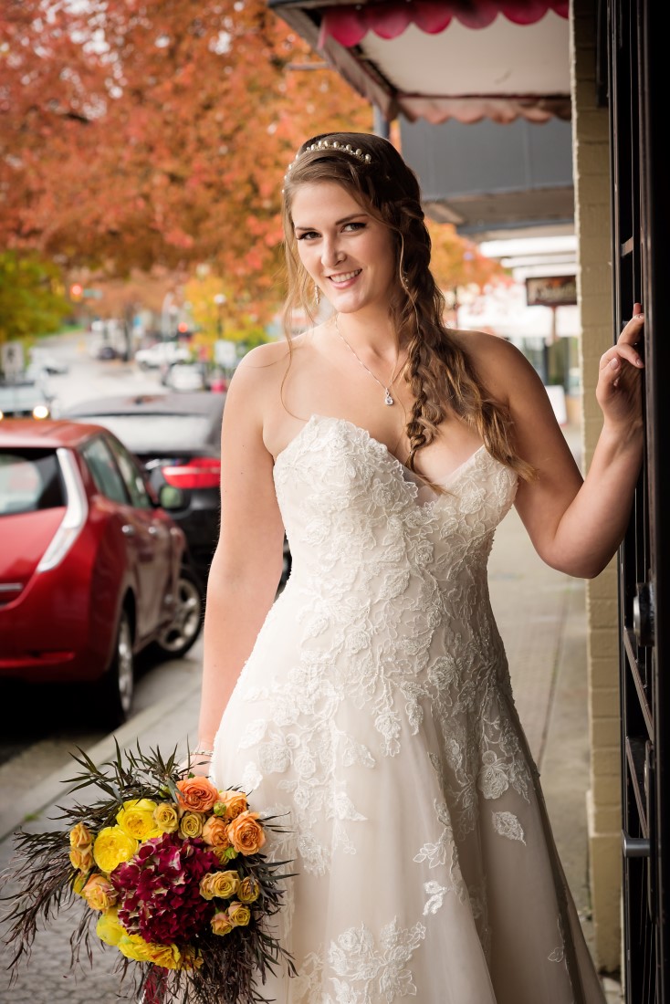 Bride poses in strapless ballgown holding orange, yellow and red bouquet