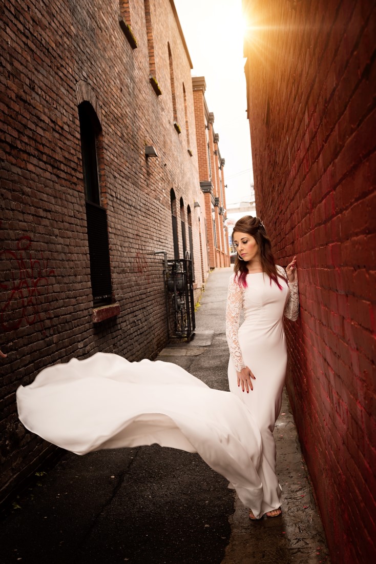 Bride in fitted gown and train flowing in alley