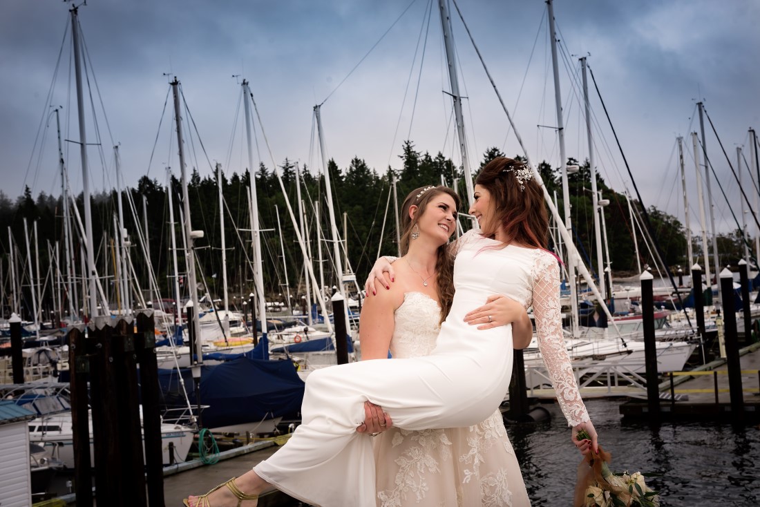 Bride lifts fellow bride in her arms in front of Nanaimo marina