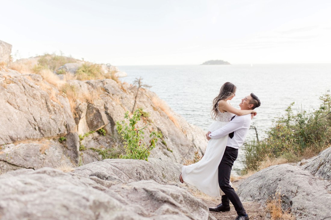 Man lifts up his fiancee and swings her around in front of ocean sunset