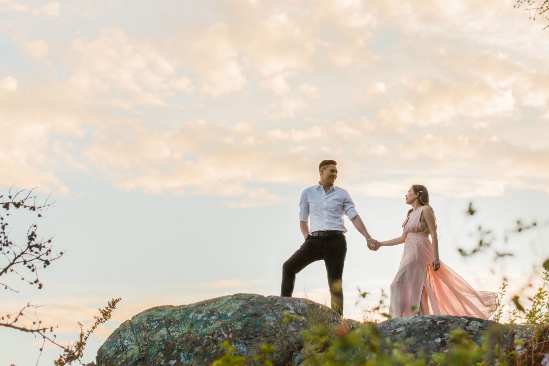 Couple holding hands climb hill with sunset behind by Vivian Ng