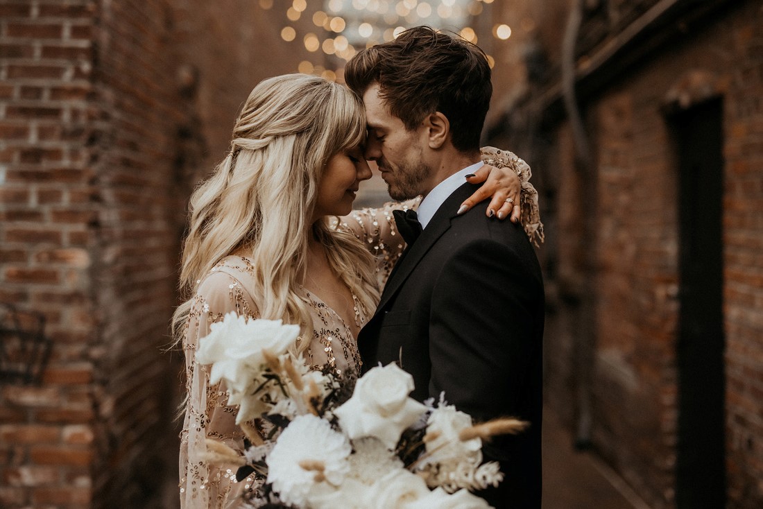 Newlyweds in Fan Tan Alley Vancouver Island hold white floral bouquet under cafe lights