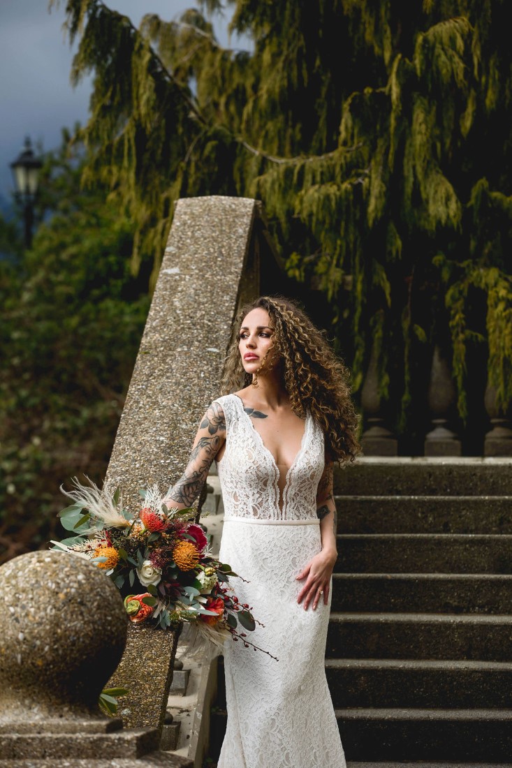 Bride in stunning gown with colourful bouquet stands on stairs of Swaneset Vancouver