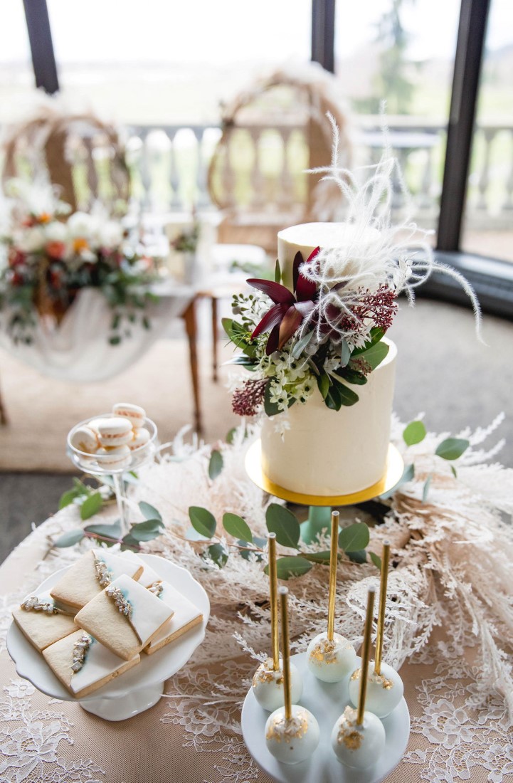 Wedding Cake with purple flowers sits on nuetral tone table by The Cake and the Giraffe Vancouver