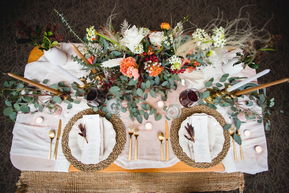 White plates on wicker place settings and flowers with pampas grass behind