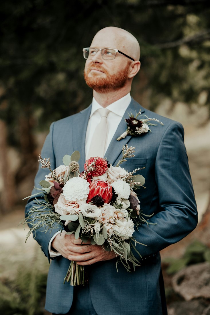 Groom holds bouquet of red and white flowers