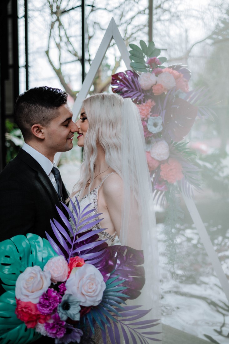 Newlyweds kiss in front of floral arrangement by En Vied Events