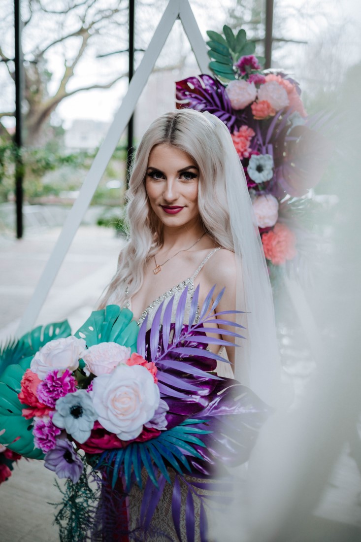 Bride holds couquet of teal, pink and white peonies and anemones by En Vied Events