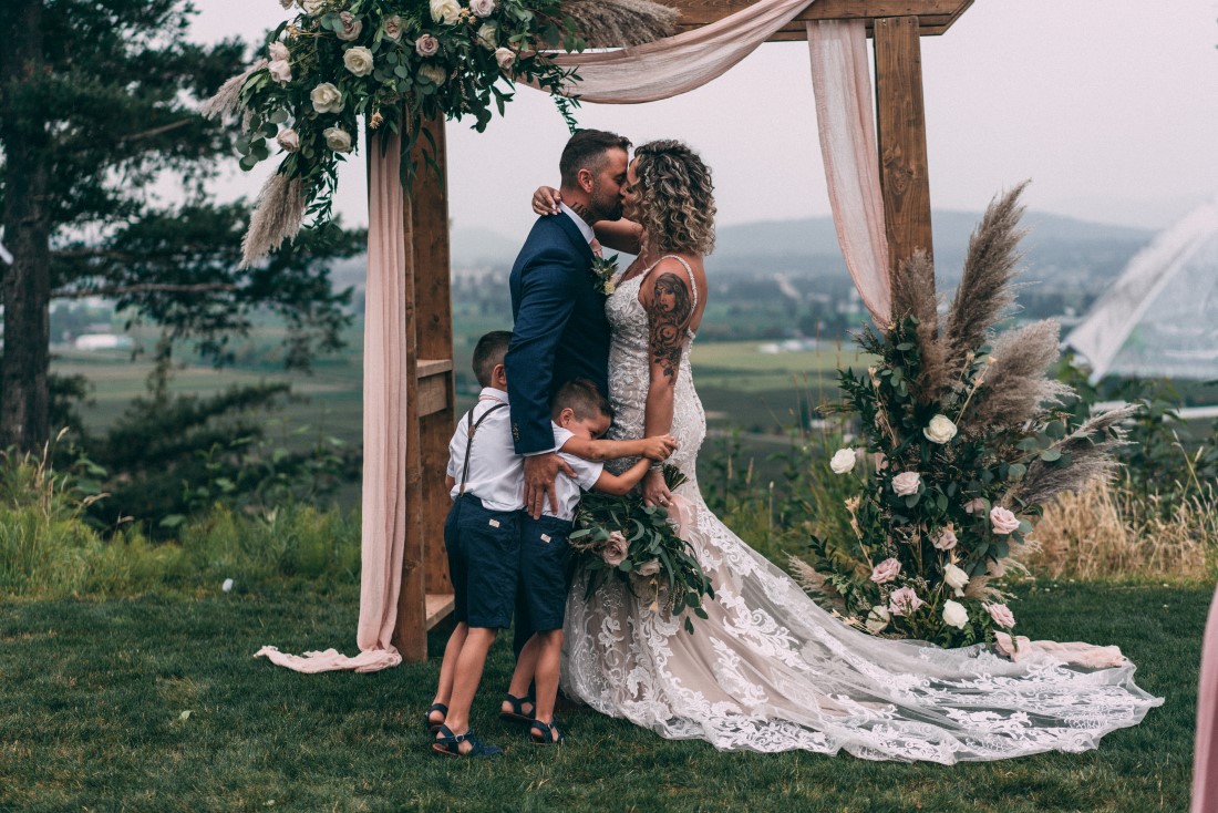 Love and Family Wedding couple kiss in fromt of weed backdrop covered in flowers