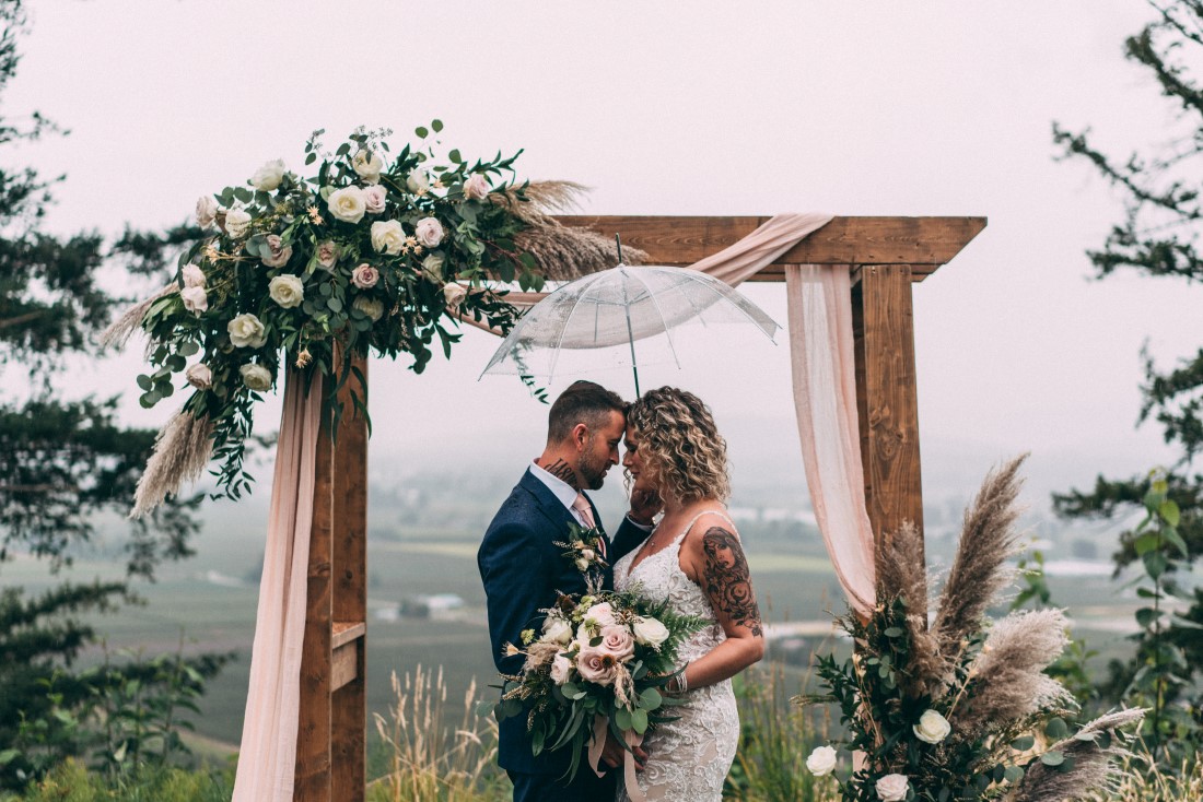 Newlyweds stand in front of wood backdrop with mountains behind