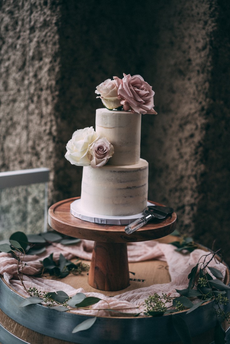 Two tier white wedding cake with pink flowers on wood pedestal by Cake First Vancouver