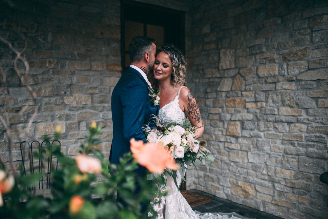 Newlyweds pose in front of rock wall by The MacLeans Photography