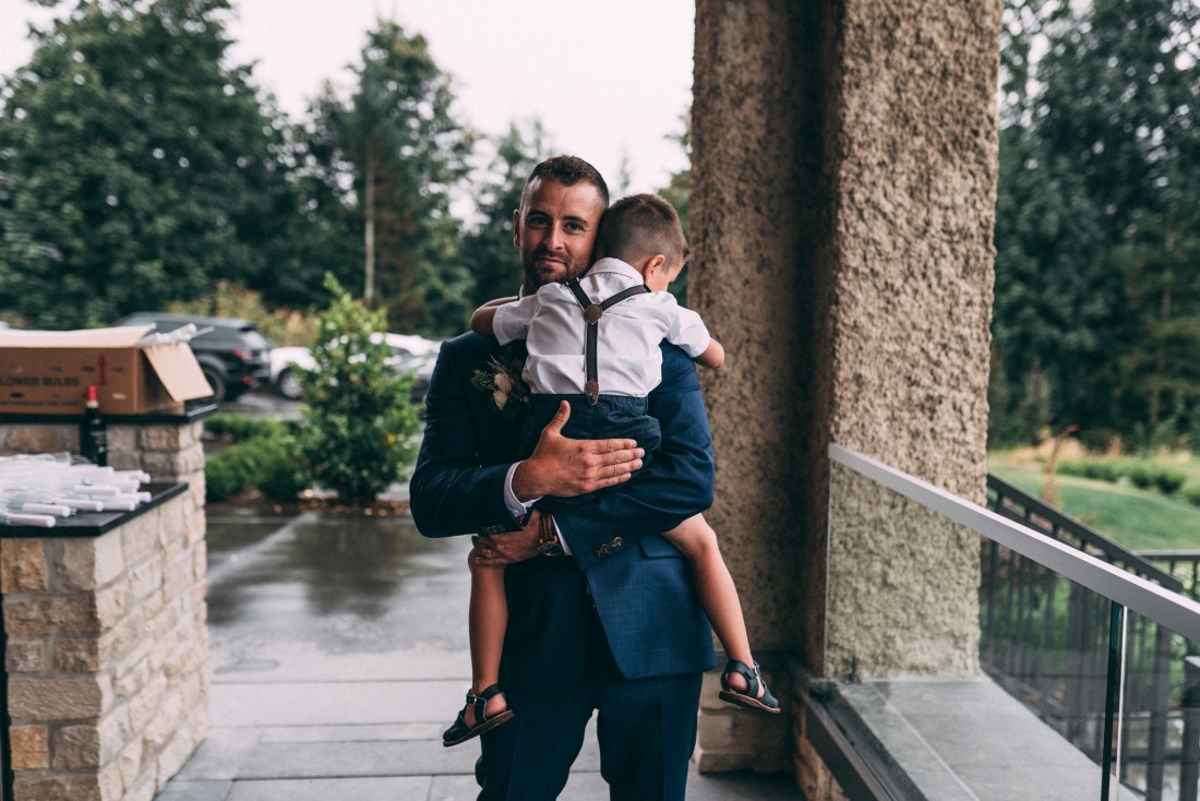 Groom holds tired young boy on wedding day