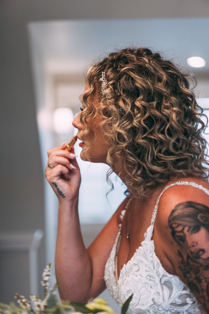 Bride puts on liptstick in mirror by MacLean Photography