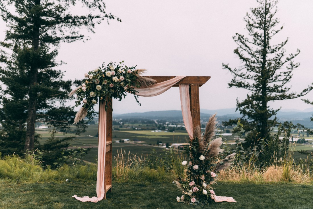 Wood ceremony backdrop covered in white fabric and floral with mountains behind by AJR Floral Design Vancouver