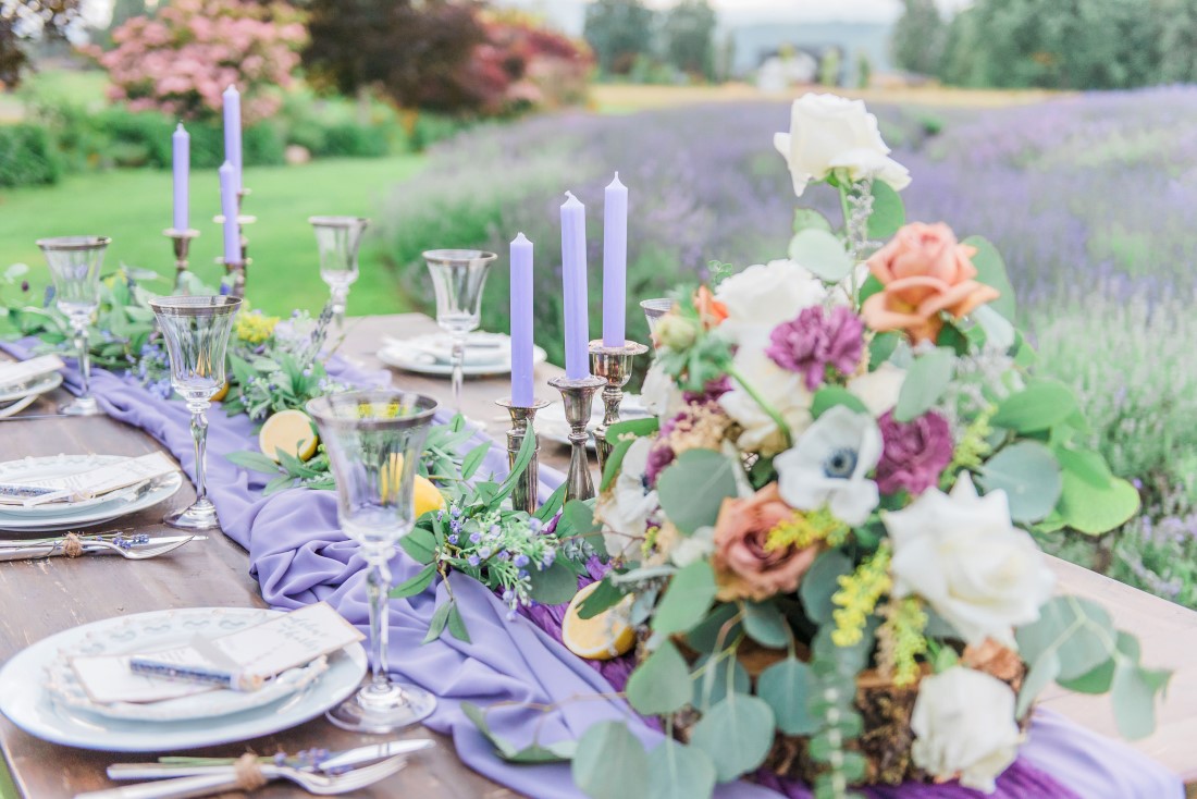 Lavender runner and candles among brightly coloured flowers on wood talbe in lavender field by Vancouver