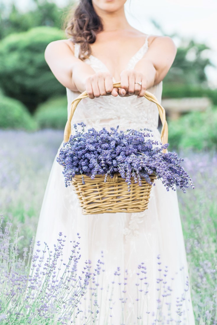 Bride in Pronovias gown holds out basket of lavender