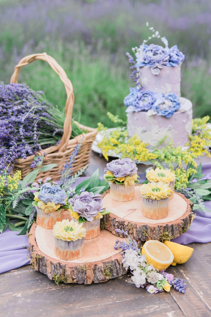 Cake, cupcakes and lavender sit on wood rounds on wedding reception table