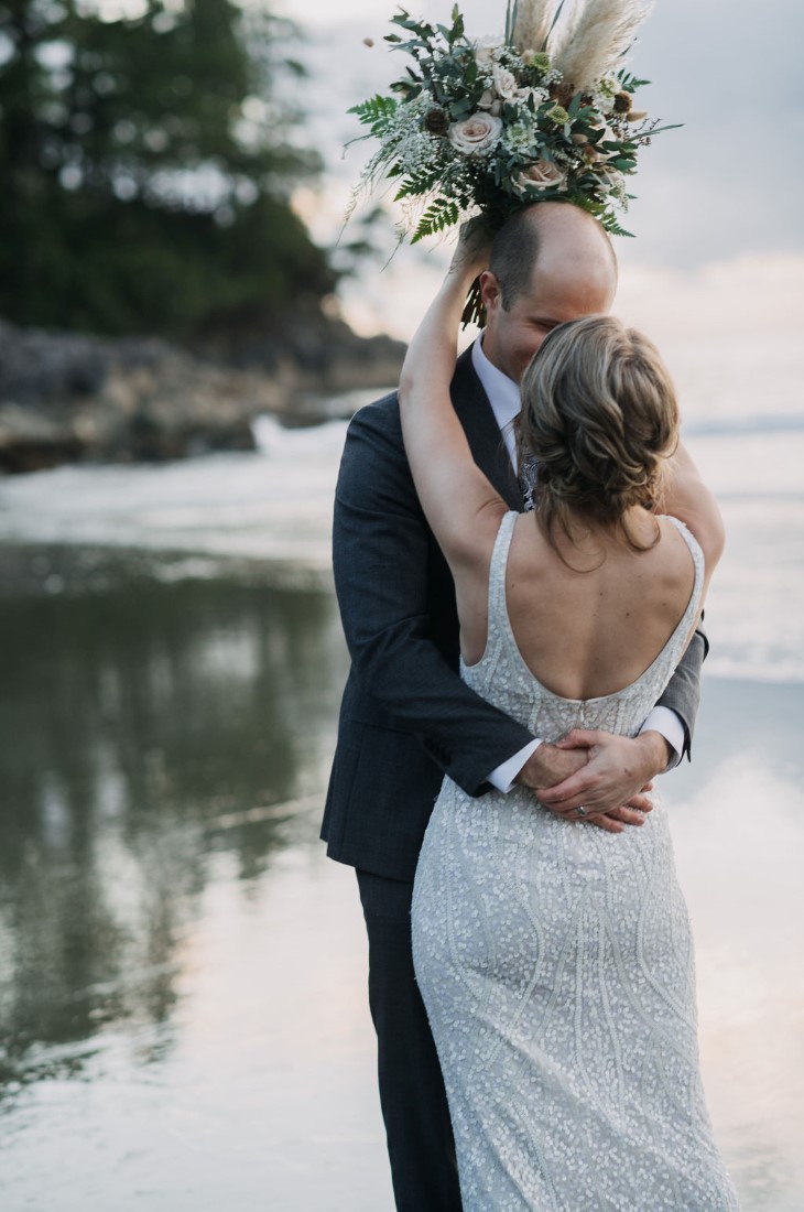 Newlyweds kiss with bouquet behind grooms head in Tofino British Columbia wedding