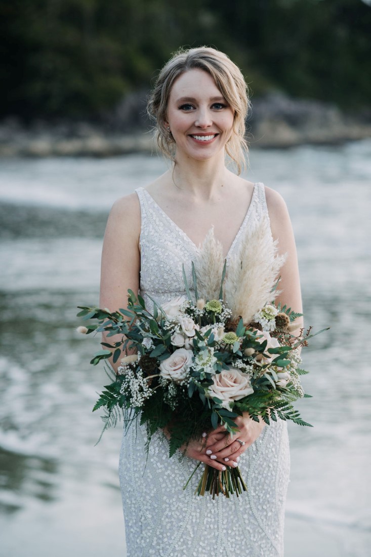 Bride in lace gown holds bouquet of ferns and roses by Crab Apple Floral Tofino