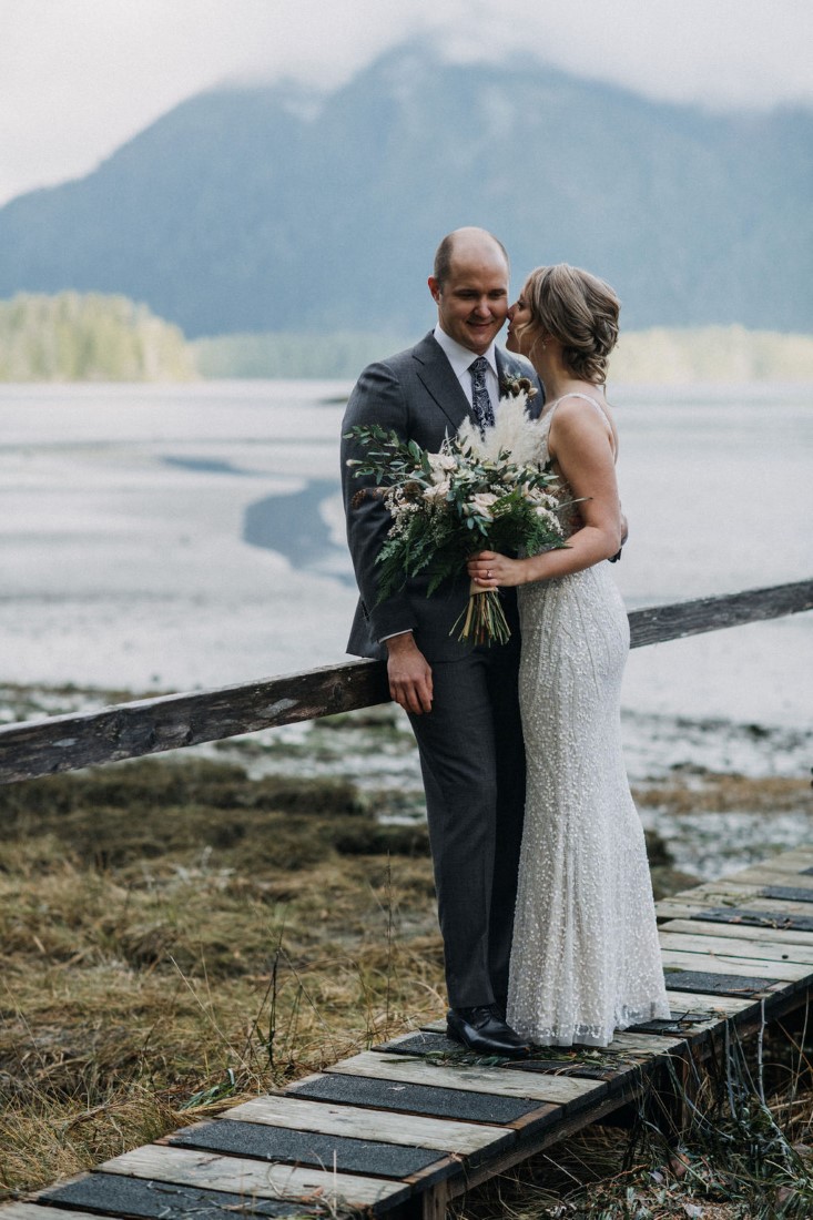 Newlyweds stand on wood sidewalk near Cedarwood Cove Tofino