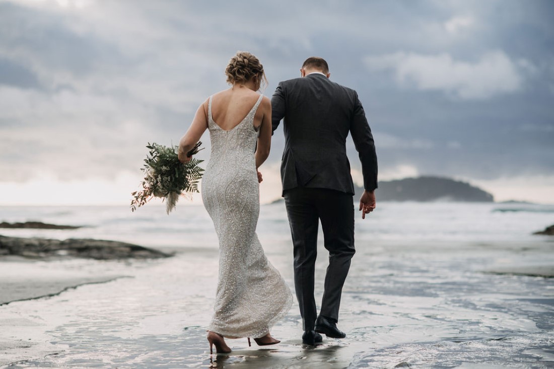 Newlyweds walk across the waves on Tofino Beach near Cedarwood Cove Cabin