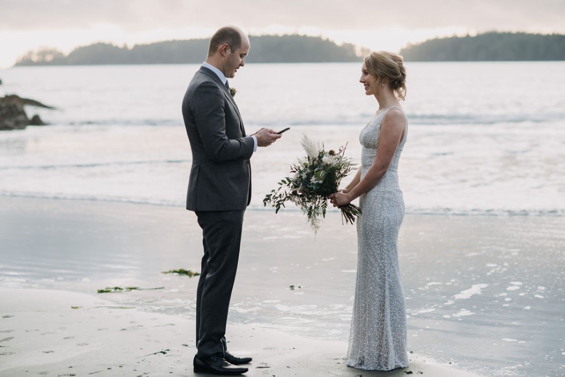 Groom reads his wedding vows to bride on Tofino beach by Bracey Photography