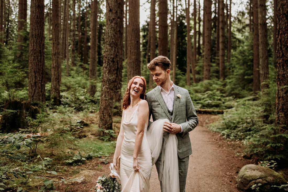 Wedding couple walk along forest path and smile at one another