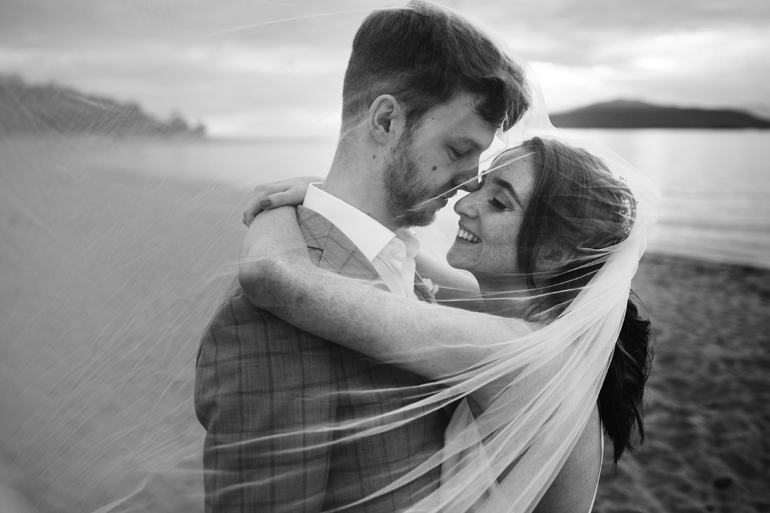 Black and white photo of bride and groom embracing on the beach